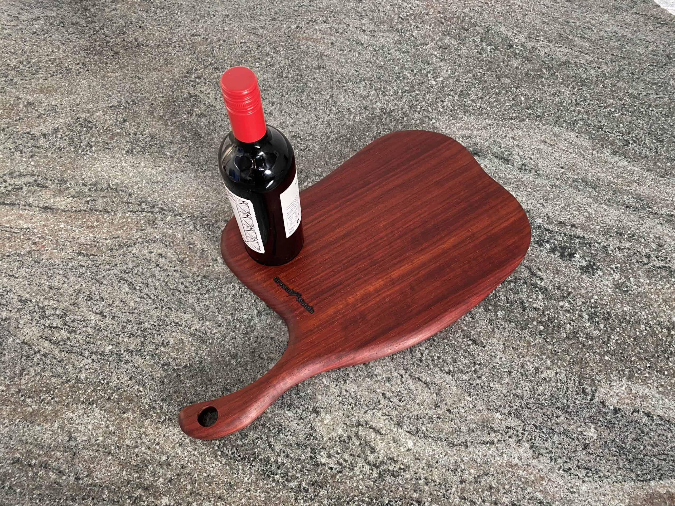 Curved Meat Cleaver Charcuterie Board in Padauk Wood 6 Birds eye view of this Slender Curved Meat Cleaver Style Charcuterie Board in Exotic Padauk Wood, with a scolloped indent to take a glass or wine bottle, showing a bottle of wine on the serving board, handcrafted by Crystal Woods and branded with their logo stamp
