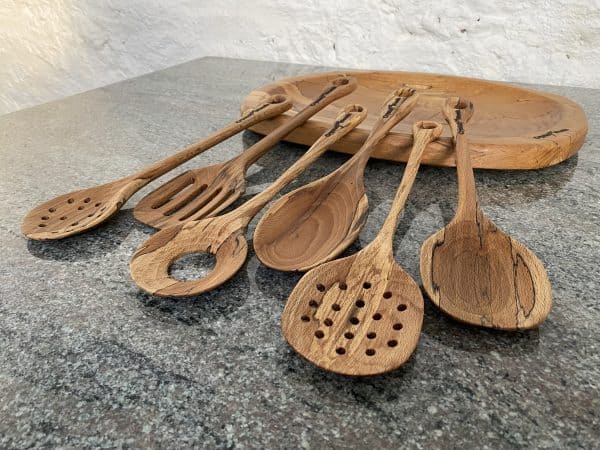 Close up angled view of this Luxury Set of 6 Spalted Beech wooden serving spoons, including an egg catcher, a slotted spoon and two strainer spoons, handcrafted by Crystal Woods from locally sourced wood in Devon, finished in food safe oil