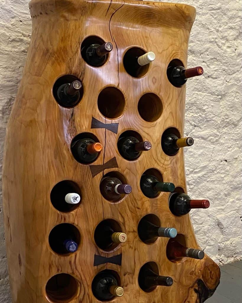 20 Battle Tree Trunk Lebanese Cedar Wine Rack with African Panga Panga bow ties finished in multiple coats of oil and displaying full bottles of wine in the holes.