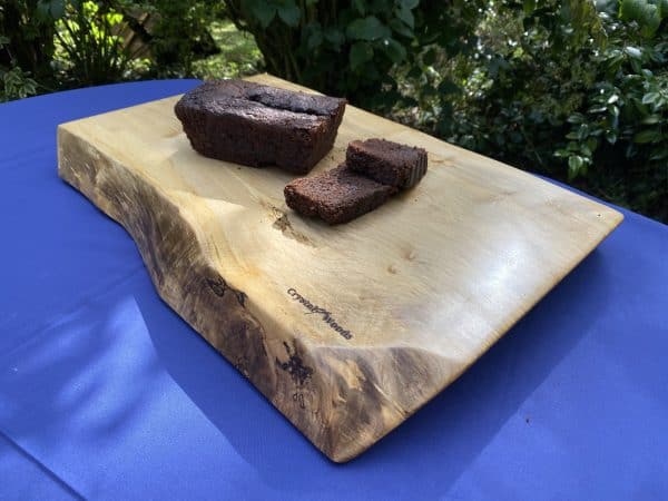 Live edge Sycamore chopping board, displaying a homemade chocolate cake, handcrafted by Crystal Woods, branded with their logo stamp