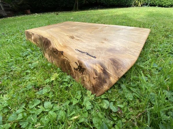 Close up angled view of this Live edge Sycamore chopping board, handcrafted by Crystal Woods, branded with their logo stamp