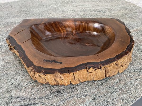 Side view of this Handmade English Walnut Sculptured Reservoir Bowl with live edge detail, created by Crystal Woods, finished in danish oil, branded with their logo stamp