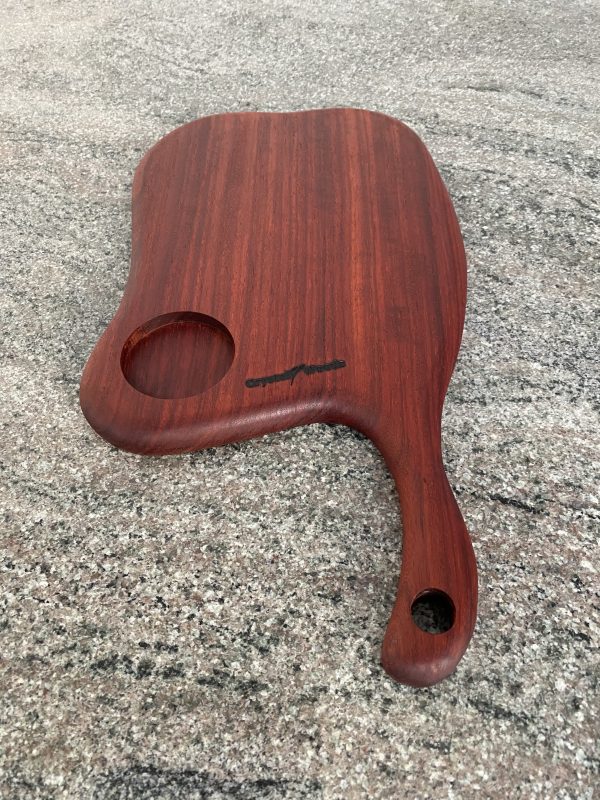 Close up view of this Slender Curved Meat Cleaver Style Charcuterie Board in Exotic Padauk Wood, with a scolloped indent to take a glass or wine bottle, handcrafted by Crystal Woods and branded with their logo stamp