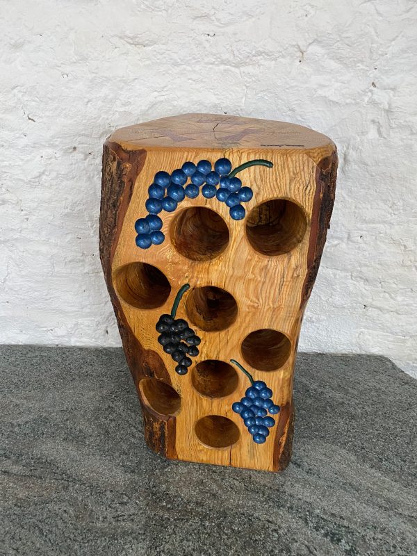 Front view of an English Ash tree stump wine rack showing all 8 empty holes, with 3 sets of engraved bunches off grapes on the front