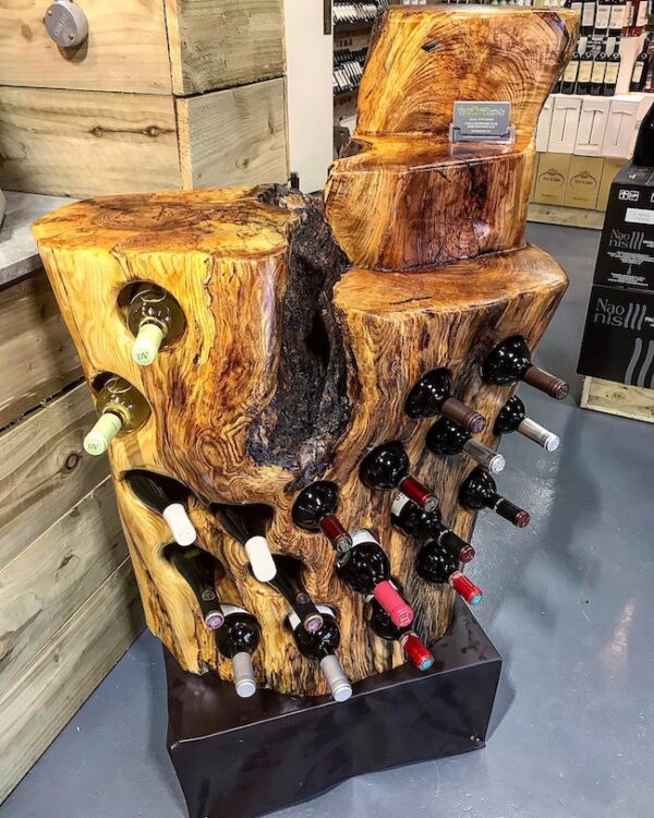 Close up view of a Tree stump driftwood wine rack on display in a wine shop, full with bottles, made from spalted ash with holes for 19 bottles, preserved and finished in multiple coats of oil, handcrafted by Crystal Woods